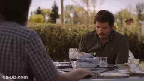 A Man With A Mustache Is Sitting At A Table With Plates And Glasses Of Wine . GIF