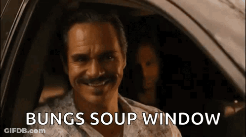 A Man With A Mustache Is Sitting In A Car With The Words Bungs Soup Window Written On The Screen Behind Him . GIF