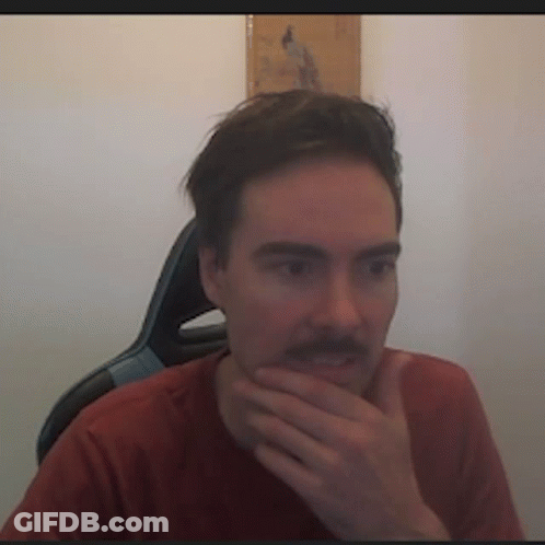 A Man With A Mustache Is Sitting In A Chair With His Hand On His Chin . GIF