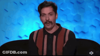 A Man With A Mustache Is Sitting In Front Of A Blue Wall GIF