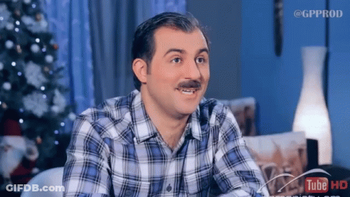 A Man With A Mustache Is Sitting In Front Of A Christmas Tree And A Sign That Says Tube Hd GIF