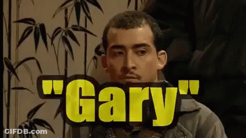 A Man With A Mustache Is Sitting In Front Of A Sign That Says Gary . GIF