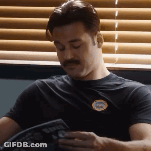 A Man With A Mustache Is Sitting In Front Of A Window Reading A Book . GIF