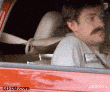 A Man With A Mustache Is Sitting In The Driver 'S Seat Of A Red Car On Peacock GIF