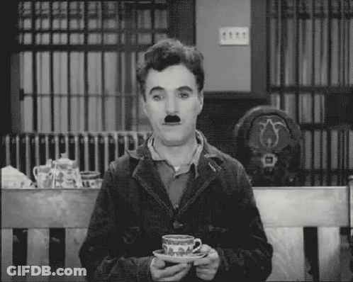A Man With A Mustache Is Sitting On A Bench Holding A Cup Of Tea . GIF