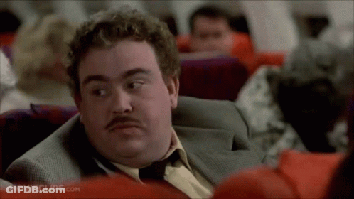 A Man With A Mustache Is Sitting On An Airplane Looking At Something . GIF