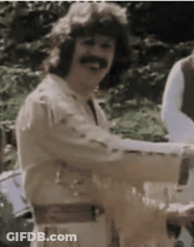 A Man With A Mustache Is Smiling And Holding A Glass Of Wine GIF