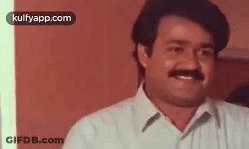 A Man With A Mustache Is Smiling And Looking At The Camera In A Room . GIF
