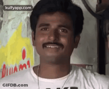 A Man With A Mustache Is Smiling For The Camera While Wearing A White Shirt . GIF