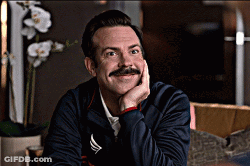 A Man With A Mustache Is Smiling With His Hand On His Chin While Wearing A Nautica Jacket GIF