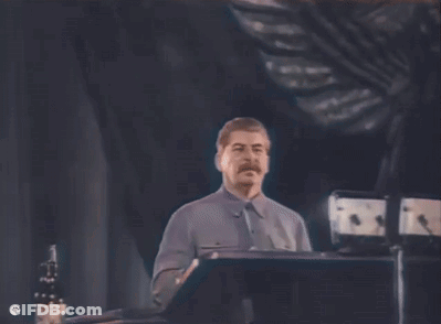 A Man With A Mustache Is Standing At A Podium Giving A Speech In A Dark Room . GIF