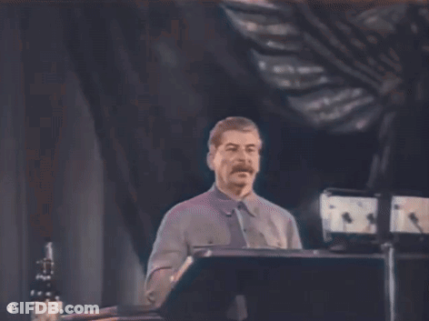 A Man With A Mustache Is Standing At A Podium Giving A Speech In A Dark Room . GIF