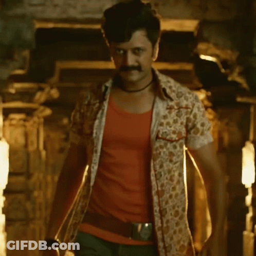 A Man With A Mustache Is Standing In A Dark Room With A Light Shining On Him GIF
