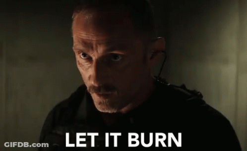 A Man With A Mustache Is Standing In A Dark Room With The Words `` Let It Burn '' Written On The Screen . GIF