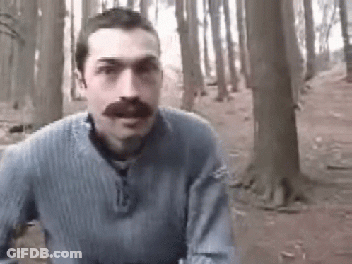 A Man With A Mustache Is Standing In A Forest . GIF