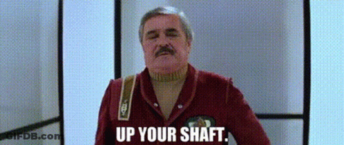 A Man With A Mustache Is Standing In A Hallway With The Words `` Up Your Shaft '' Written On The Screen . GIF