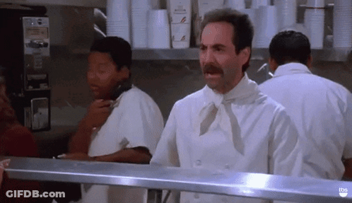 A Man With A Mustache Is Standing In A Kitchen Talking On A Phone . GIF