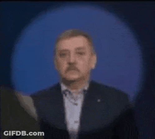A Man With A Mustache Is Standing In Front Of A Blue Light . GIF