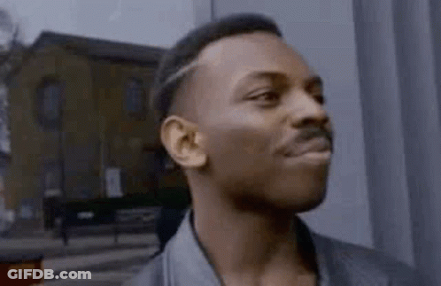 A Man With A Mustache Is Standing In Front Of A Building And Making A Funny Face . GIF