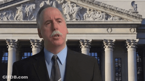 A Man With A Mustache Is Standing In Front Of A Building With Columns GIF