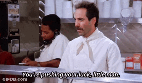 A Man With A Mustache Is Standing In Front Of A Counter In A Restaurant And Talking On A Phone . GIF