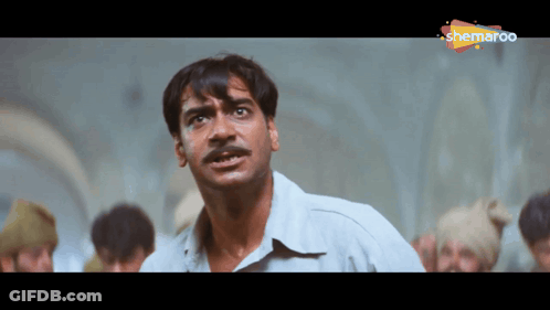 A Man With A Mustache Is Standing In Front Of A Group Of People And A Sign That Says Shemaroo On It GIF
