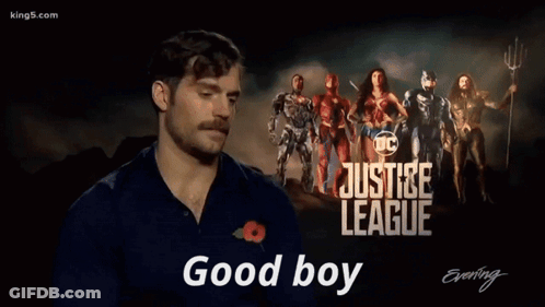 A Man With A Mustache Is Standing In Front Of A Poster For The Justice League GIF