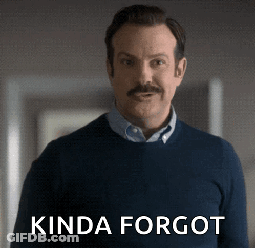 A Man With A Mustache Is Standing In Front Of A Sign That Says " Kinda Forgot " GIF