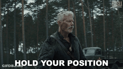 A Man With A Mustache Is Standing In The Woods And Says Hold Your Position GIF