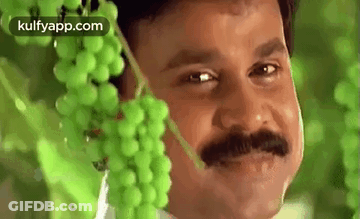 A Man With A Mustache Is Standing Next To A Bunch Of Grapes . GIF