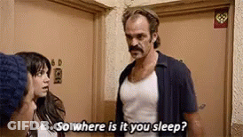 A Man With A Mustache Is Standing Next To A Woman In A Room And Talking To Her . GIF