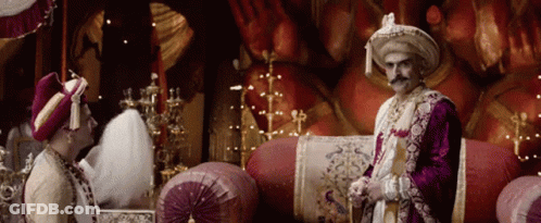 A Man With A Mustache Is Standing Next To Another Man In A Costume GIF