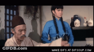 A Man With A Mustache Is Talking To A Woman In A Blue Shirt GIF