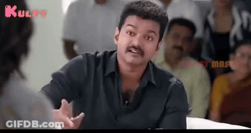 A Man With A Mustache Is Talking To A Woman While Sitting In Front Of A Crowd Of People . GIF