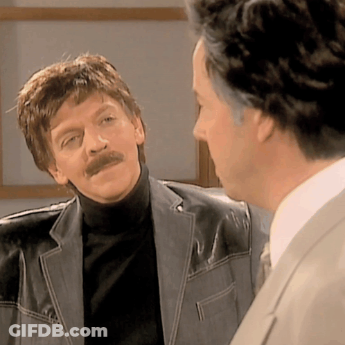 A Man With A Mustache Is Talking To Another Man GIF