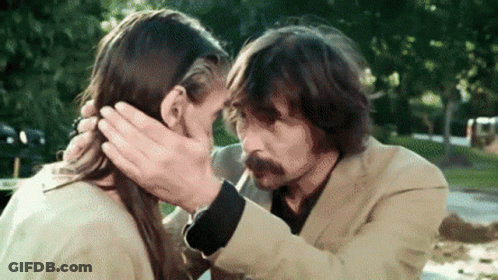 A Man With A Mustache Is Touching A Woman 'S Face . GIF
