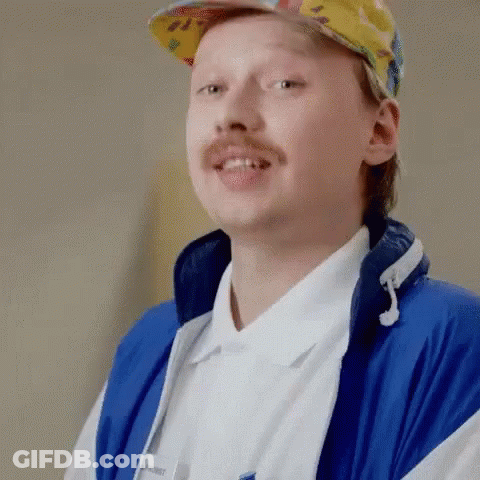 A Man With A Mustache Is Wearing A Blue Jacket And A Hat . GIF