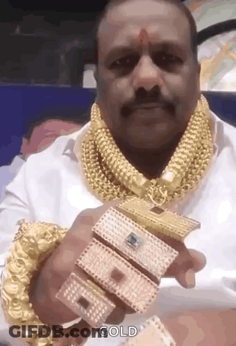 A Man With A Mustache Is Wearing A Lot Of Gold Jewelry And Holding A Bracelet . GIF