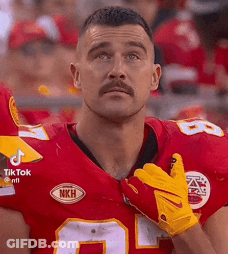 A Man With A Mustache Is Wearing A Red Jersey And Yellow Gloves While Standing In Front Of A Crowd . GIF