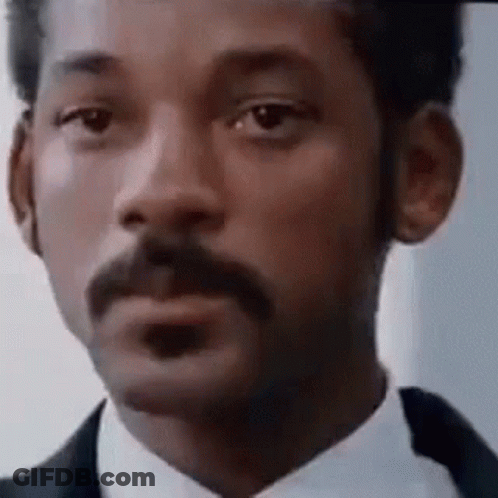 A Man With A Mustache Is Wearing A Suit And Tie And Making A Funny Face . GIF