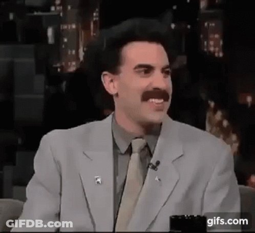 A Man With A Mustache Is Wearing A Suit And Tie And Talking On A Microphone . GIF
