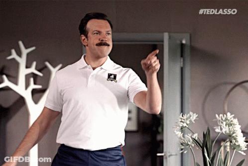 A Man With A Mustache Is Wearing A White Shirt That Says Ted Lasso On It GIF