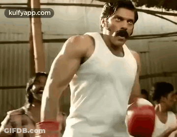 A Man With A Mustache Is Wearing Boxing Gloves And A Tank Top . GIF