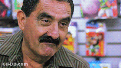 A Man With A Mustache Looks At The Camera In Front Of A Wall Of Toys GIF