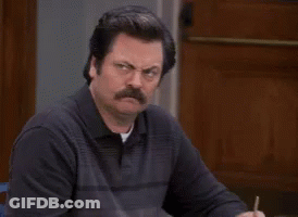 A Man With A Mustache Sits At A Table With A Pen In His Hand GIF