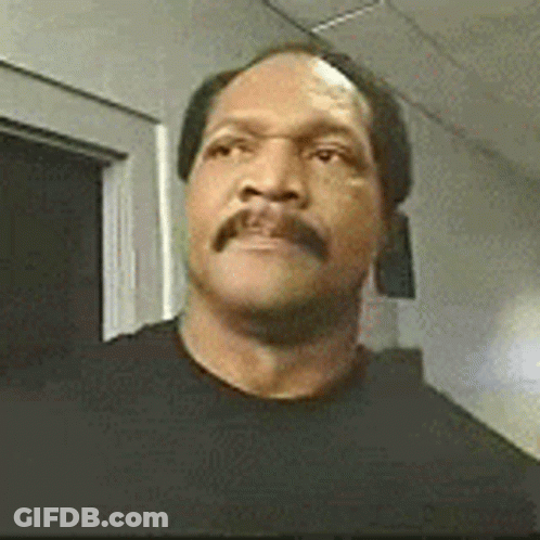 A Man With A Mustache Wearing A Black Shirt Is Standing In A Hallway . GIF