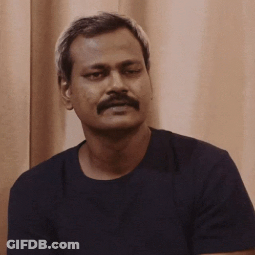 A Man With A Mustache Wearing A Black Shirt Looks At The Camera GIF