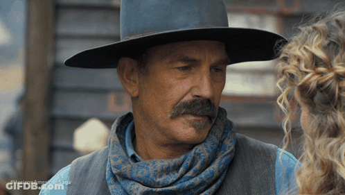 A Man With A Mustache Wearing A Cowboy Hat And Scarf Talks To A Woman In A Horizon American Saga Ad GIF