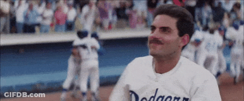 A Man With A Mustache Wearing A Dodgers Jersey Is Standing On A Baseball Field . GIF