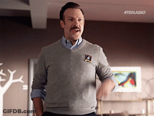 A Man With A Mustache Wearing A Grey Sweater And A Blue Shirt GIF